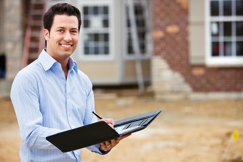 Image of a real estate agent for new construction standing in front of a construction site.