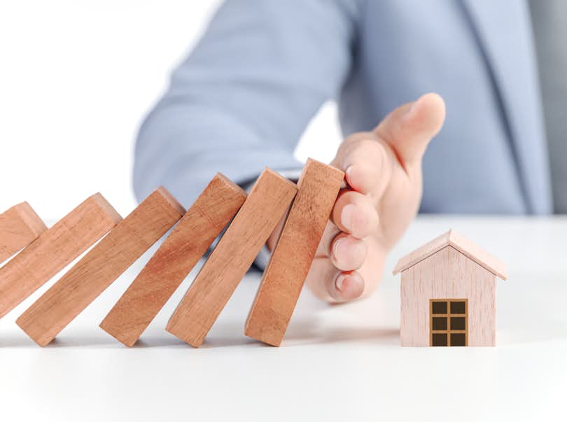 Hand stops dominoes from hitting model of house