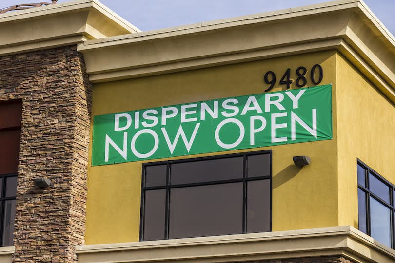 Exterior of building announcing that a dispensary is now open using a green and white sign