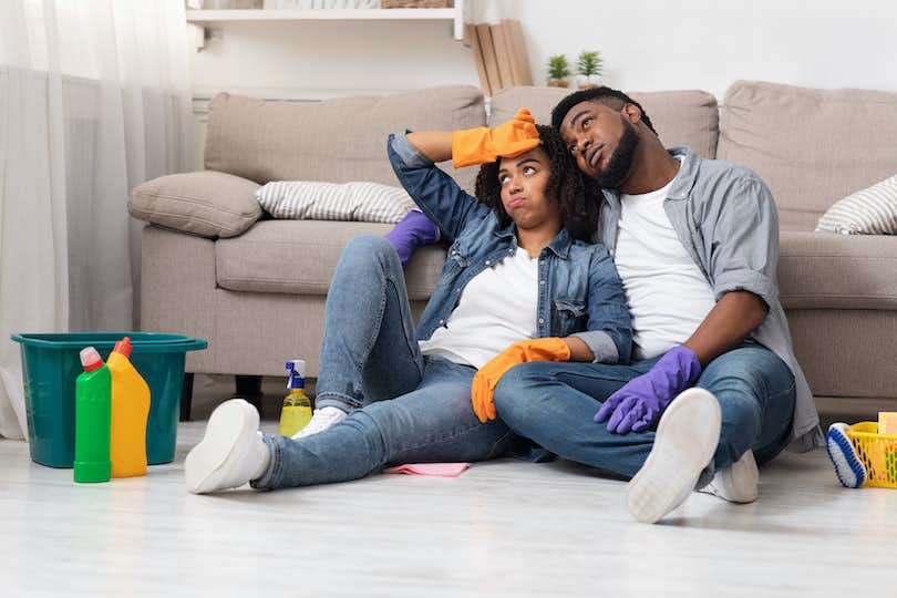 exhausted couple sitting on the floor surrounded by cleaning products and home improvement supplies