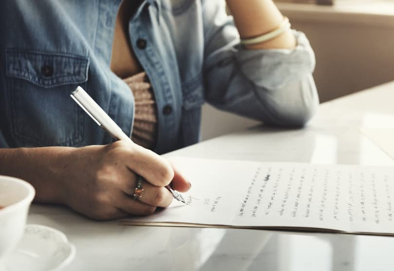 Woman's hand holds a pen as she writes a letter.