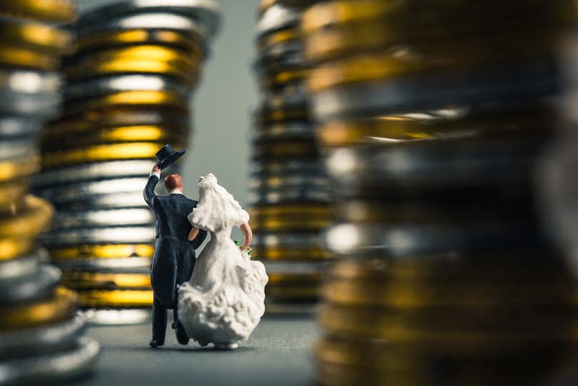 photo of toy figures of a bride and groom walking on the road, surrounded by piles of coins to convey debt being a dealbreaker marriage decline
