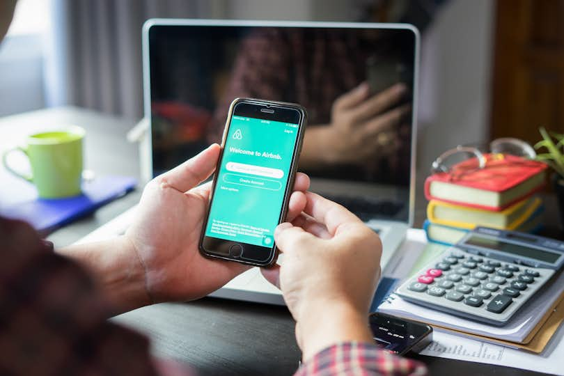 a man holds a smartphone with the screen featuring the Airbnb login page