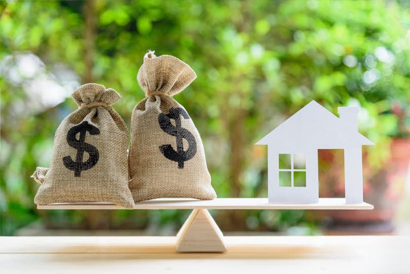Money balanced on a scale with a house to represent home equity. Here's how to calculate equity.