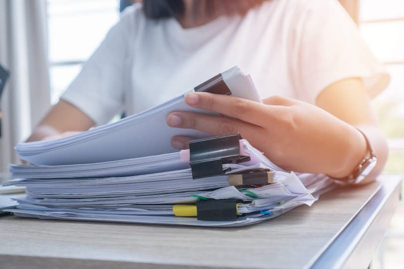 Woman with stack of documents on desk goes through underwriting process