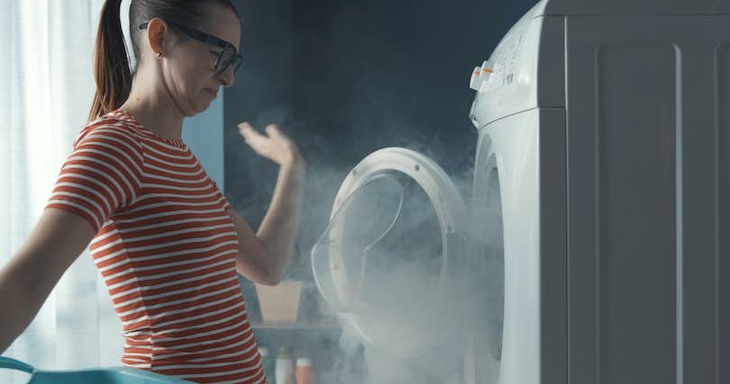 woman waves her hand to clear away smoke coming from her clothes dryer