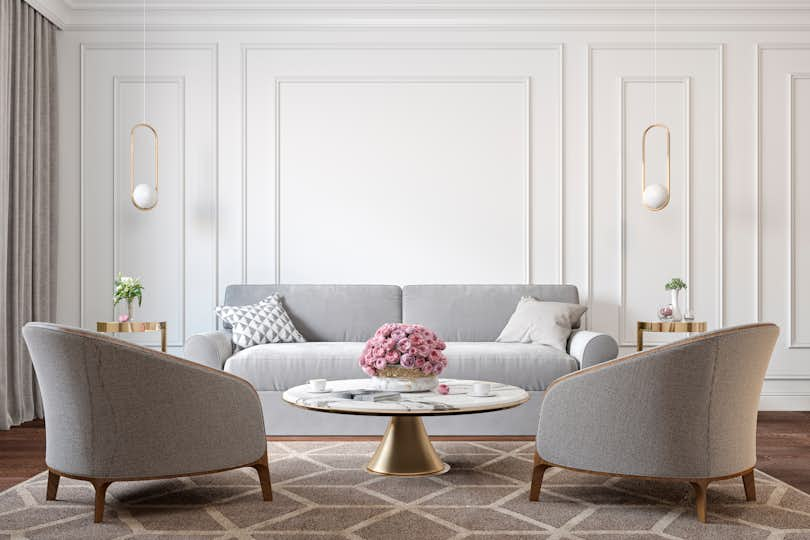 Art deco interior with gray armchairs, sofa, marble coffee table, lamps, carpet, flowers and wall moldings