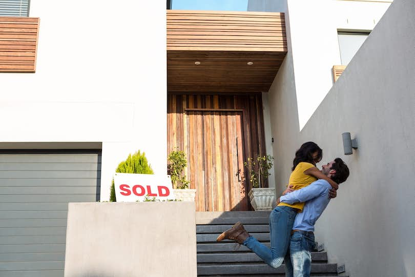 Young couple celebrates in front of their new home purchased with a first time homebuyer program