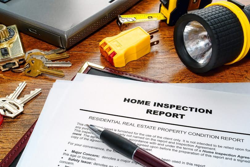 Home inspection report surrounded by pen, keys, and flashlight