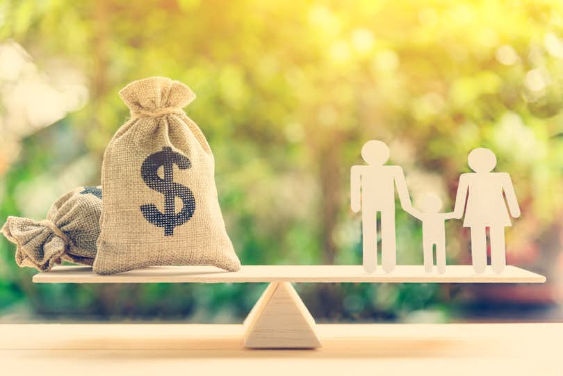 Money saving for kids, family financial wealth management concept : Dollar or cash in hemp bags or burlap sacks and a white paper cut (dad, mom and son) on wood balance scale. Green nature background.