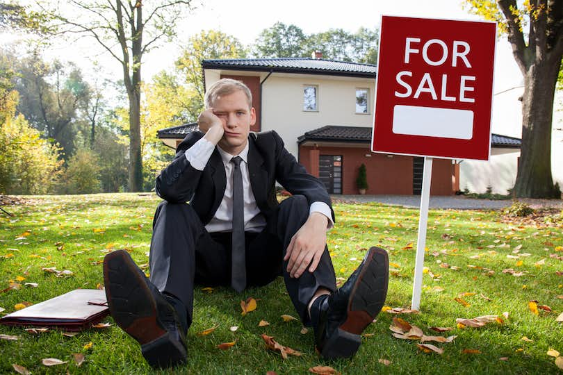 Dejected man sits on front lawn next to a house 