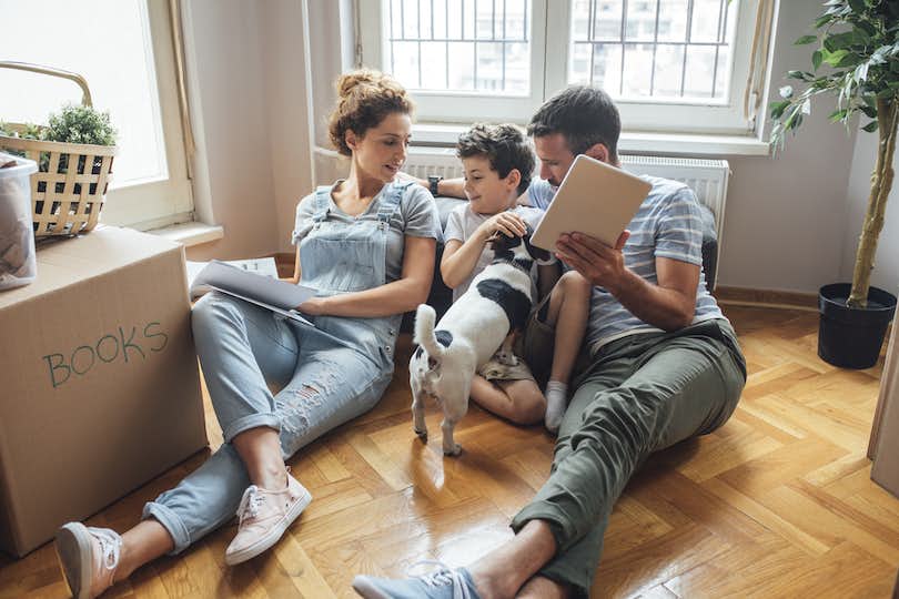 Family with dog sit on floor of new home next to boxes.