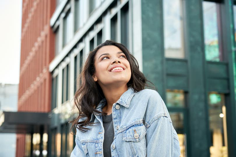 Teenaged girl looks hopefully at the sky with buildings behind her