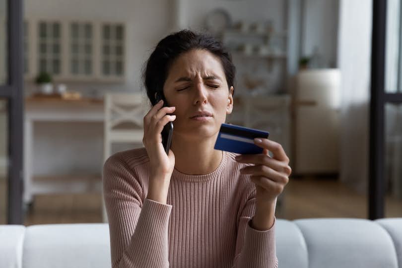 Woman with pained expression holding a credit card and phone