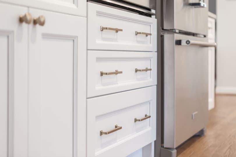 White kitchen built with shaker style cabinets featuring polished copper handles