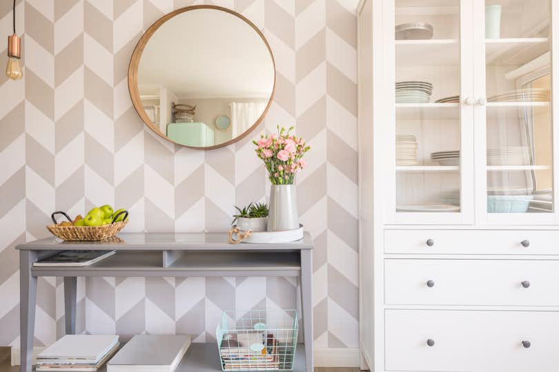 Mirror on patterned wallpaper above gray table with flowers in scandi living room interior