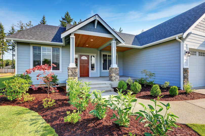 house with stone columns, concrete walkway, and newly mulched flower beds