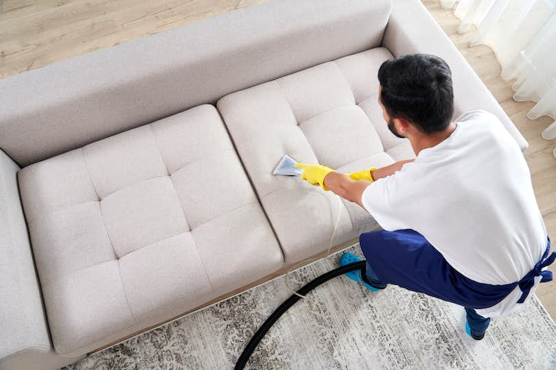 Close-up of housekeeper holding modern washing vacuum cleaner and cleaning dirty sofa with professional detergent