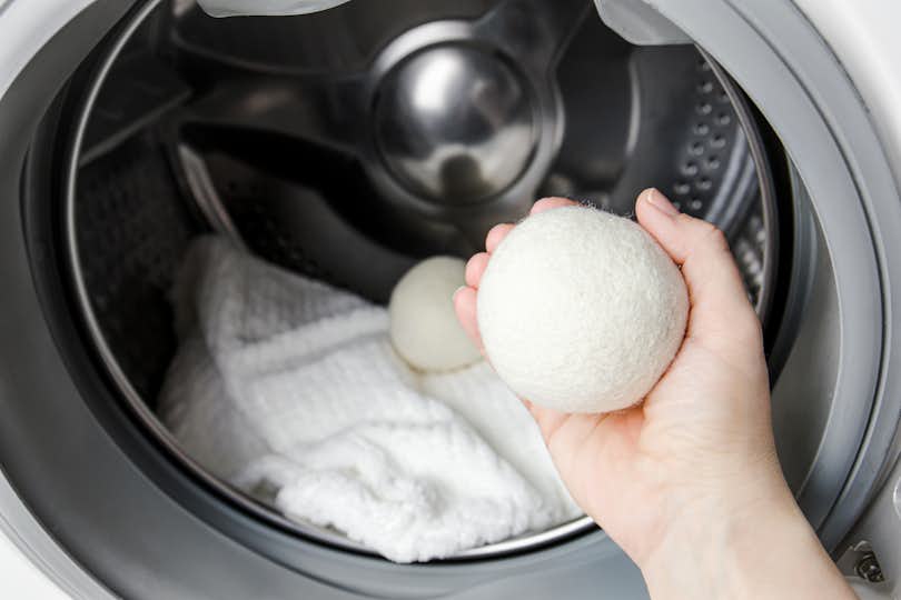 hand holding a dryer ball in front of an open clothes dryer